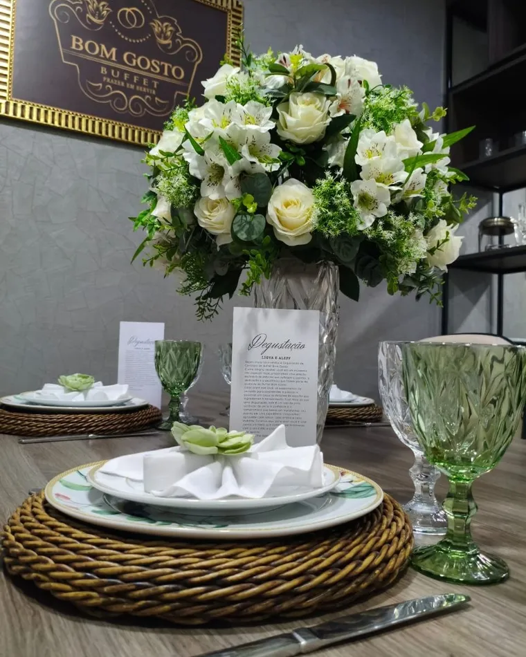 Mesa de degustação posta com louça branca, sousplat e arranjo central de flores
