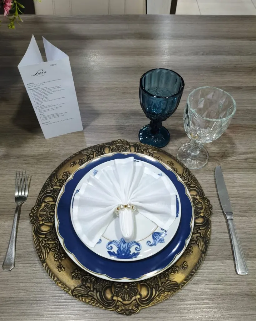 Detalhe de mesa posta com prato azul, sousplat dourado e taças de cristal