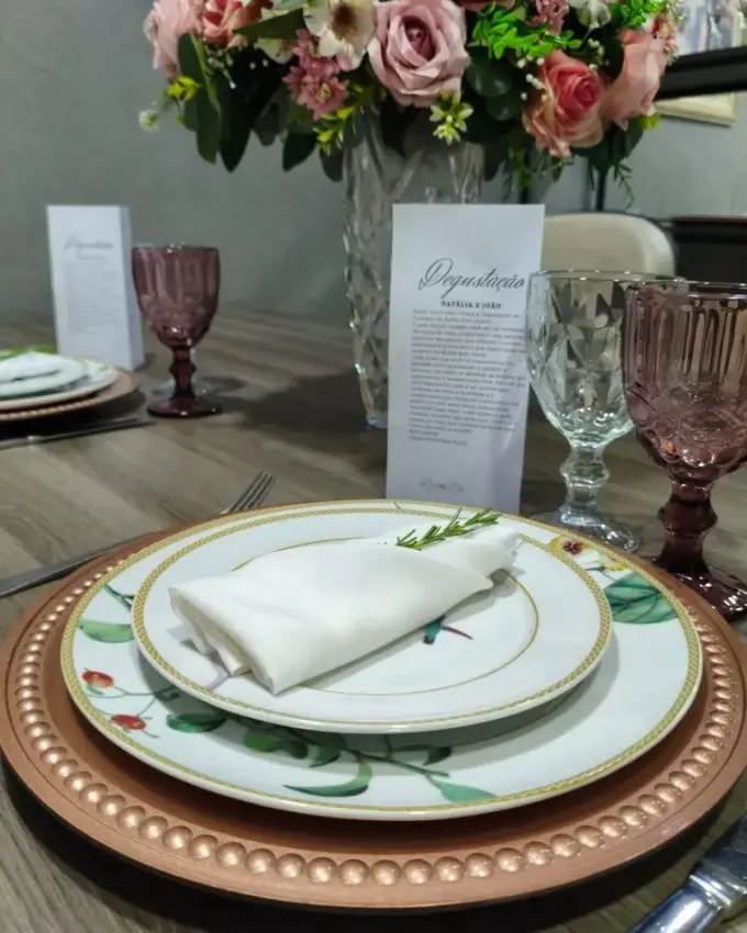 Mesa de degustação posta com louça branca, cristais verdes e arranjo de flores
