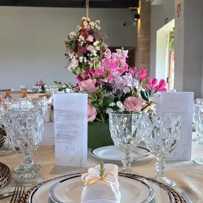 Mesa de casamento posta em um salão, com louça, taças de cristal e arranjo de flores