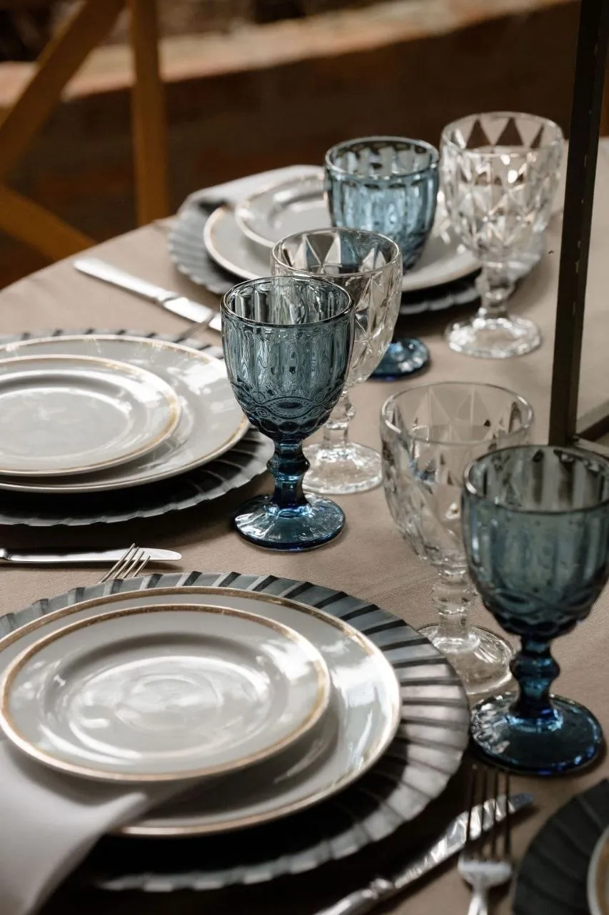 Mesa posta em azul marinho, com taças de cristal, sousplat e pratos com filete dourado