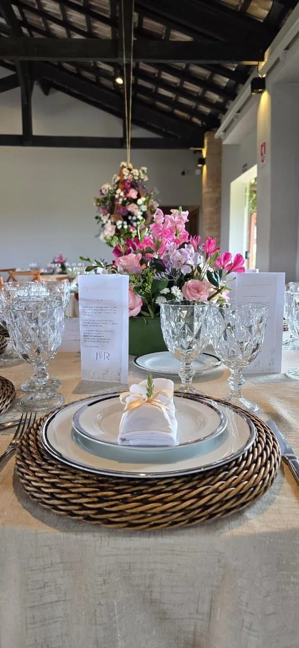 Mesa posta com sousplat de fibra rattan trançado, louça com filete e arranjo de flores
