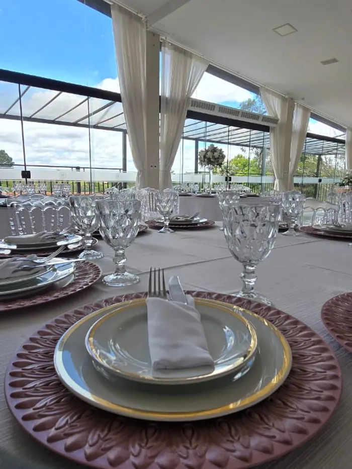 Mesa posta em tom rosa, com sousplat, louça e taças de cristal